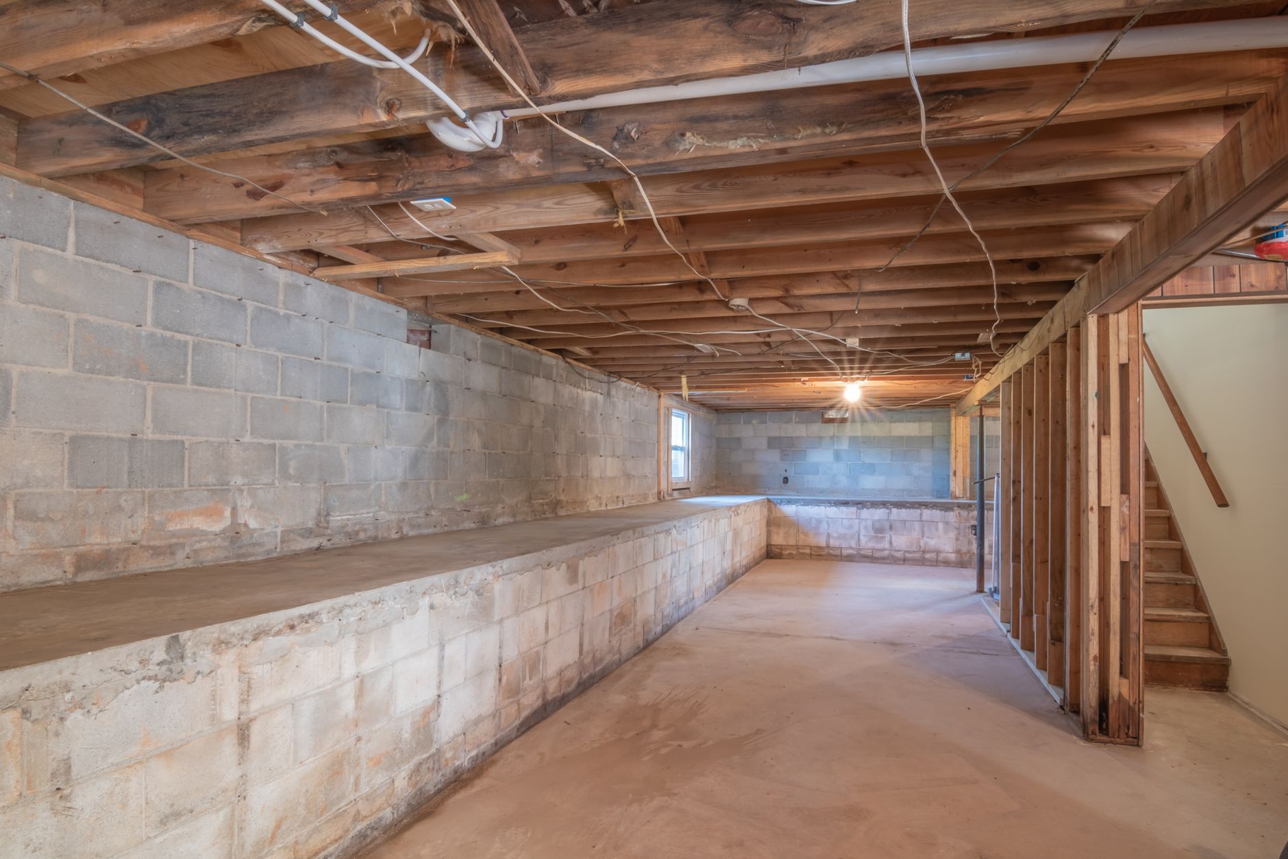 Empty basement with exposed wooden beams, concrete walls and stairs